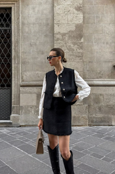 a  lady wears a black tweed vest with matching mini skirt and boots